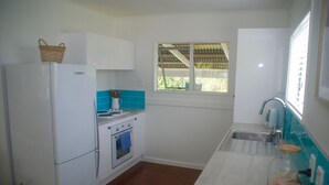 Cozinha compacta com eletrodomésticos brancos, uma janela e vista para o verde lá fora.