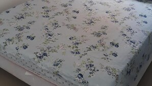A bed with a floral bedspread and matching pillow, a window with curtains, and a plain wall.