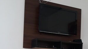 A flat-screen TV mounted on a wooden panel above a black entertainment unit.
