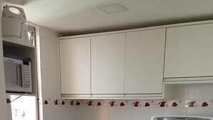 A kitchen with white cabinets, a black countertop, a refrigerator, a microwave, and a stove. There are two black chairs at the counter.