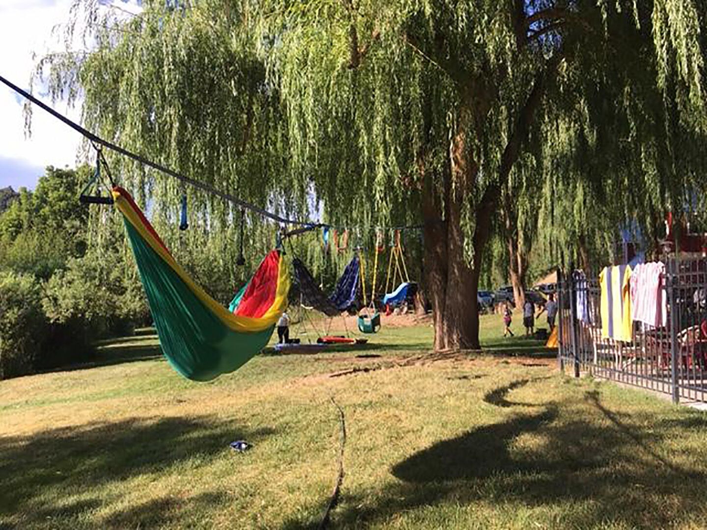 A hammock swing set in a park with trees and a fenced area.