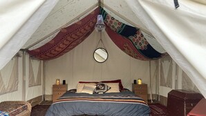 Una habitació còmoda i de forma triangular, en estil de tenda, amb un llit, dues taules de nit, una làmpada penjant i un petit mirall rodó.