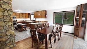 A spacious kitchen with wooden cabinets, a large island, and a dining area with a wooden table and chairs. - Private pool. On the river. A few summer dates left in 2027. And, 2028 Now Open. (Preston)