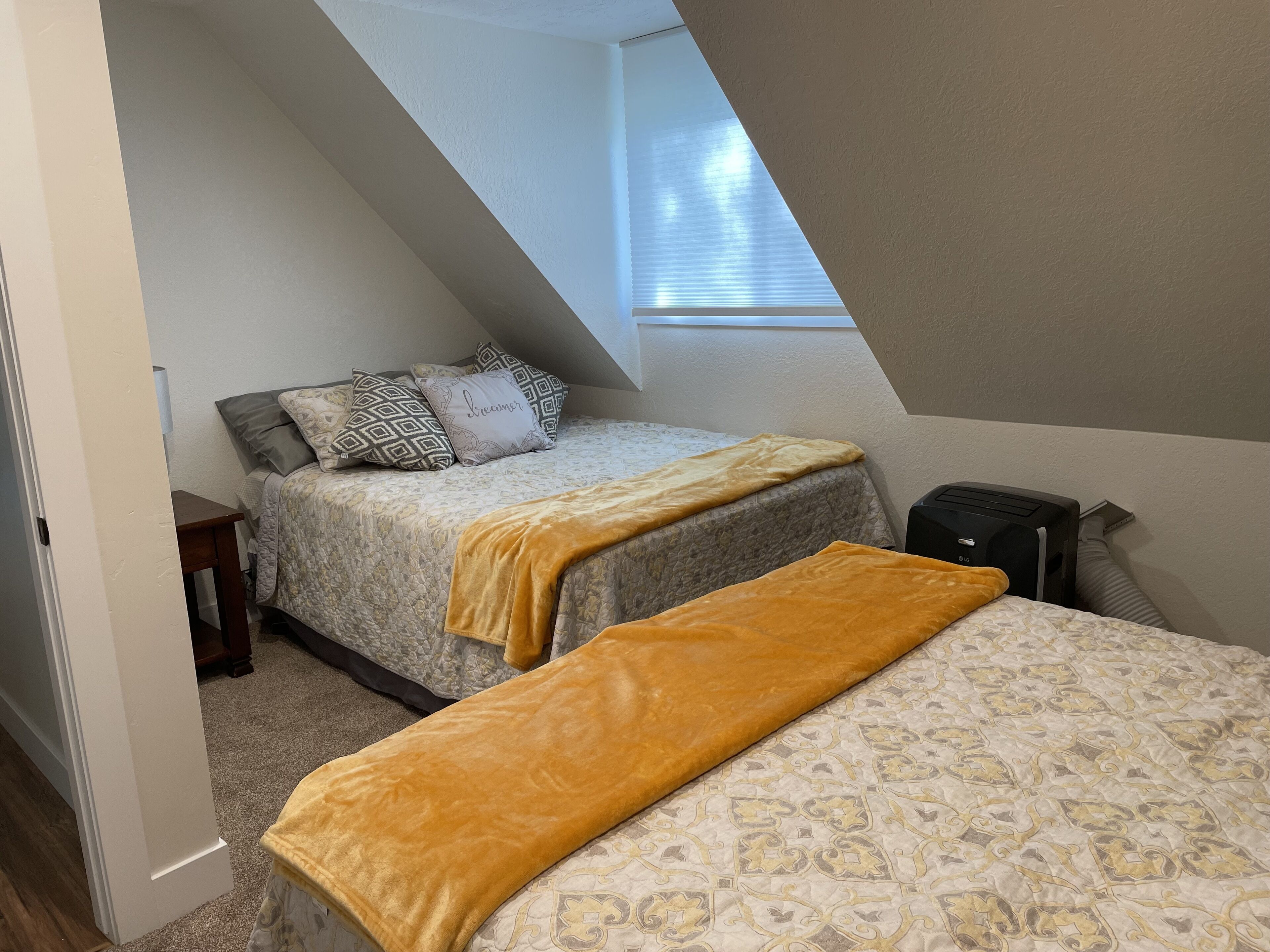 Une petite pièce agréable, avec un plafond en pente, deux lits dotés de draps à motifs, une table de chevet et un radiateur.