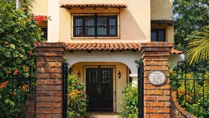 A two-story building with a thatched roof, a brick entrance gate, and a paved pathway leading to the entrance. - Acogedora palapa privada cerca de la playa. (Puerto Escondido)