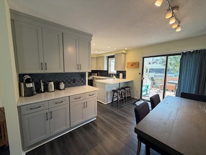 A modern kitchen with grey cabinets, a large island, and a dining area with a wooden table and chairs. - Spacious 3BR End Unit Townhome with Pool, 3 Blocks to Beach (Bethany Beach)