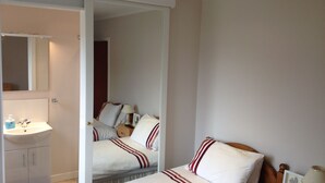 Habitación de hotel con cama, mesita de noche, lámpara y baño con lavamanos y espejo.
