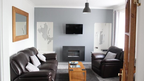 Una sala de estar moderna con chimenea, dos sofás de cuero, una mesa de centro y un televisor montado.