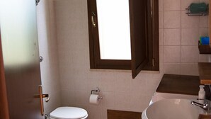 A bathroom with a toilet, sink, and a window with a wooden frame. - APARTMENT IN CASTIADAS BETWEEN SEA AND MOUNTAINS (cagliari)