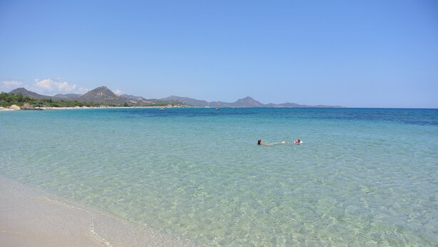 A beach with clear turquoise water, a sandy shore, and distant mountains. - APARTMENT IN CASTIADAS BETWEEN SEA AND MOUNTAINS (cagliari)