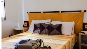 A neatly made bed with a striped bedspread, a gray handbag, and a pair of glasses on the bed. There are two bedside tables with lamps and framed pictures on the wall above the bed. - APARTMENT IN CASTIADAS BETWEEN SEA AND MOUNTAINS (cagliari)
