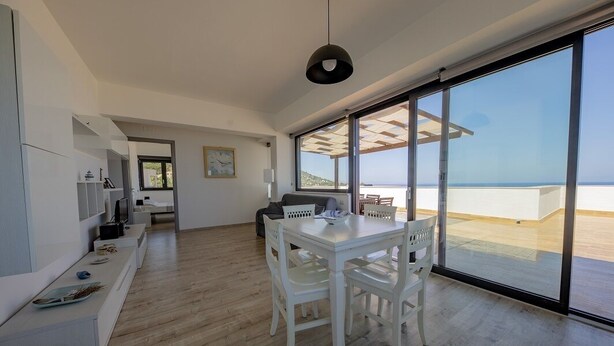 Een moderne woonkamer met een eethoek en grote schuifdeuren die uitkomen op een balkon met uitzicht op zee.