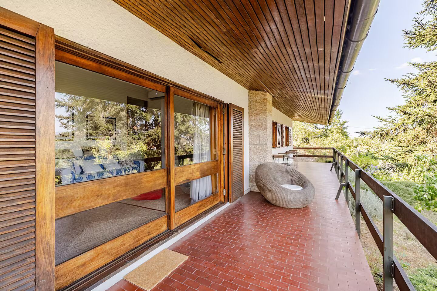 Un pati exterior modern amb un terra de fusta, una porta de vidre que dona a una habitació i una zona de seients amb una cadira rodona.