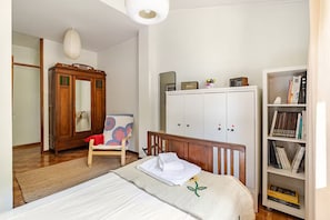 Une chambre à coucher comprenant un lit, une armoire en bois, une chaise, une bibliothèque et une commode avec un miroir.