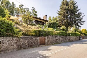 Propiedad residencial con muro de piedra, portón de madera y una carretera al frente.