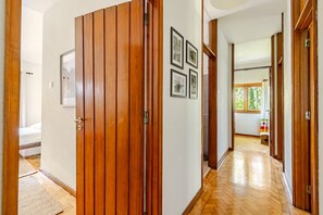 Um corredor com portas de madeira, uma cama e quadros nas paredes.