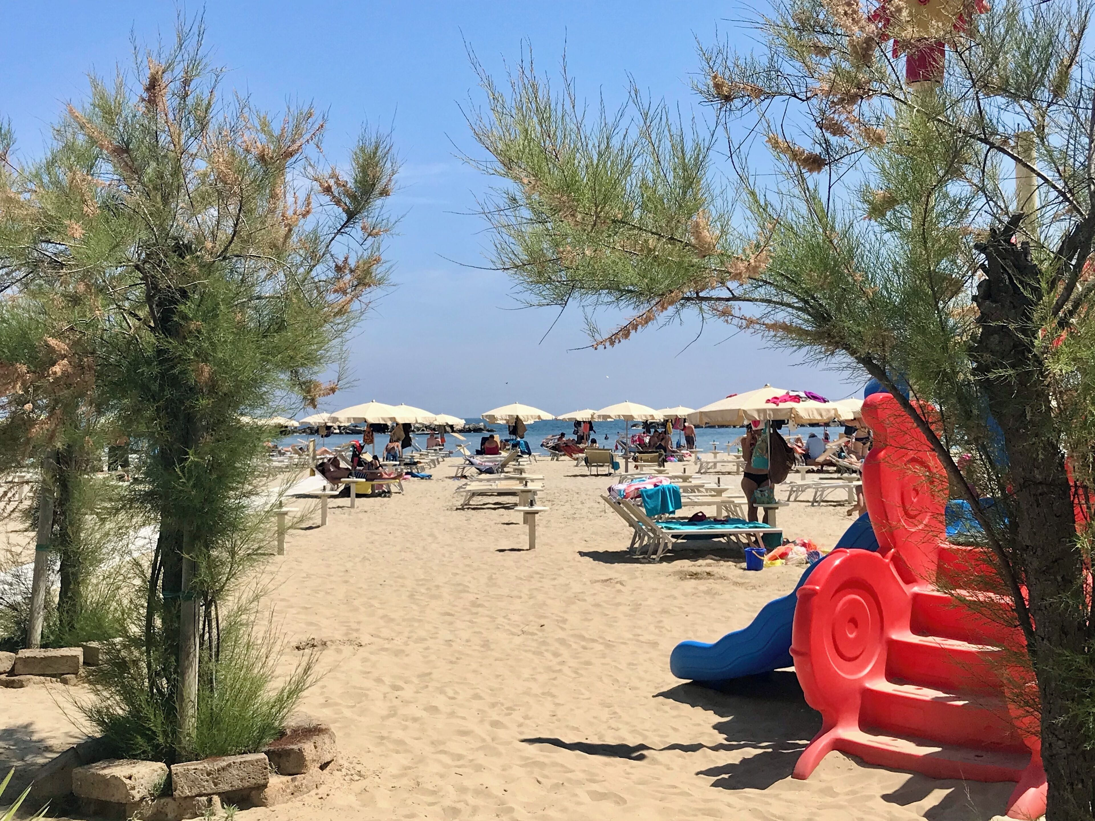 Una playa con tumbonas, sombrillas y una zona de juegos infantiles.