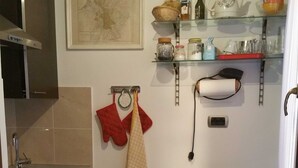 Cocina compacta con lavamanos, una mesa de comedor y sillas. Hay estantes sobre la encimera con diversos utensilios de cocina.