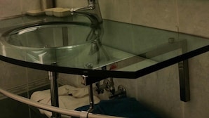 Un baño con lavamanos de vidrio, un espejo y un perchero para toallas.