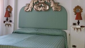 Un dormitorio con una cama verde a rayas, un cabecero decorativo, una obra de arte enmarcada sobre la cama y dos mesitas de noche con lámparas y relojes.