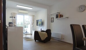 A living room with a sofa, a television, a bookshelf, and a clock on the wall.