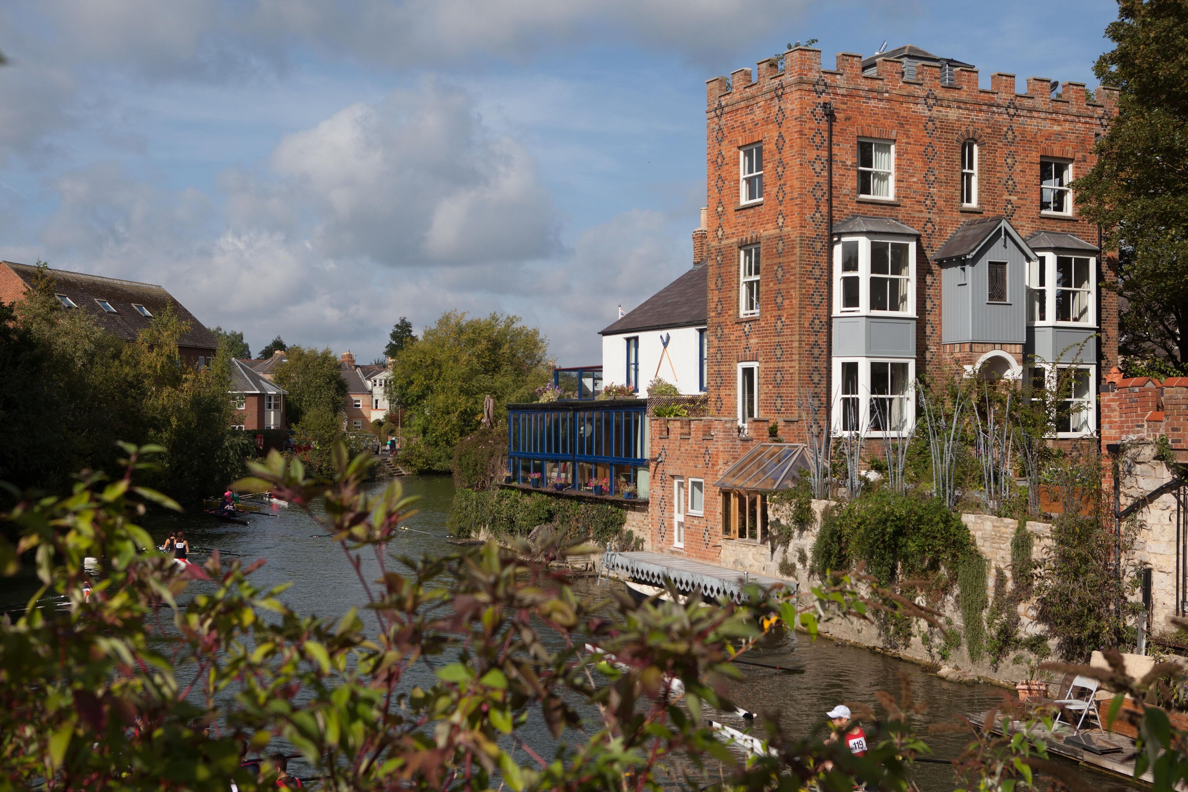 Un bâtiment situé au bord de la rivière, doté d’une tour, d’un pont et bordé par une rivière où naviguent des bateaux.