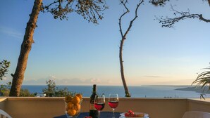A table set for two with a bottle of wine, glasses, and plates of food, overlooking a scenic view of the sea. - VILLA ALDA TWO ROOMS APARTMENT - Apartment with Enchanting View (Santa Cesarea Terme)