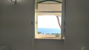 A bedroom with a bed, a window with a view of the sea, a small table, and a lamp. - VILLA ALDA TWO ROOMS APARTMENT - Apartment with Enchanting View (Santa Cesarea Terme)