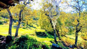 Une structure rustique en bois, agrémentée d’une lanterne suspendue, se dresse au milieu d’un paysage luxuriant et verdoyant, parsemé d’arbres et de rochers.
