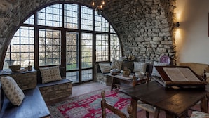 A cozy room with a stone wall, large arched windows, a wooden table, and a bench.