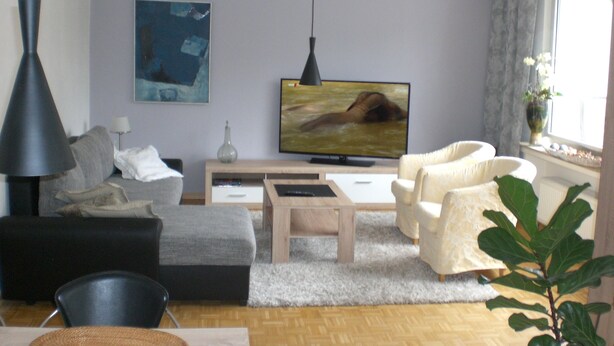 Een woonkamer met een bank, fauteuil, salontafel, televisie en een plant.