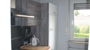 Een kleine keuken met donkere kastjes, een fornuis en een raam met uitzicht op groen.