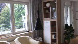Een kamer met een witte fauteuil, een houten boekenkast, een hanglamp en een plant in pot.