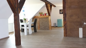 Une pièce spacieuse avec des poutres apparentes, une cheminée en briques et un coin repas comprenant une table et des chaises.