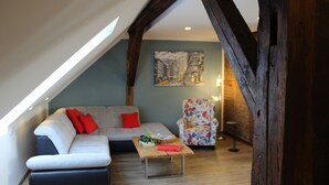 Un salon chaleureux de style industriel, avec un plafond en pente, un canapé agrémenté de coussins rouges, un fauteuil à motifs floraux et une table basse en bois.