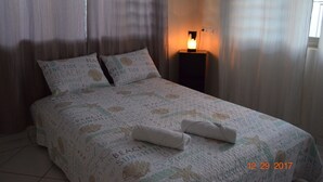 Ein ordentlich bezogenes Bett mit Strandmotiv, Nachttischlampe und einem Fenster mit Vorhängen.