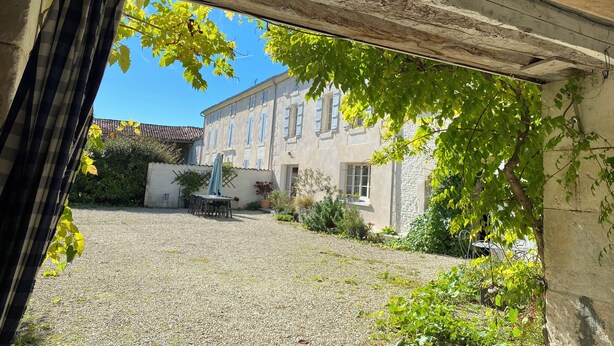 A courtyard with a gravel ground, a table and chairs, and a building with a stone facade and multiple windows.