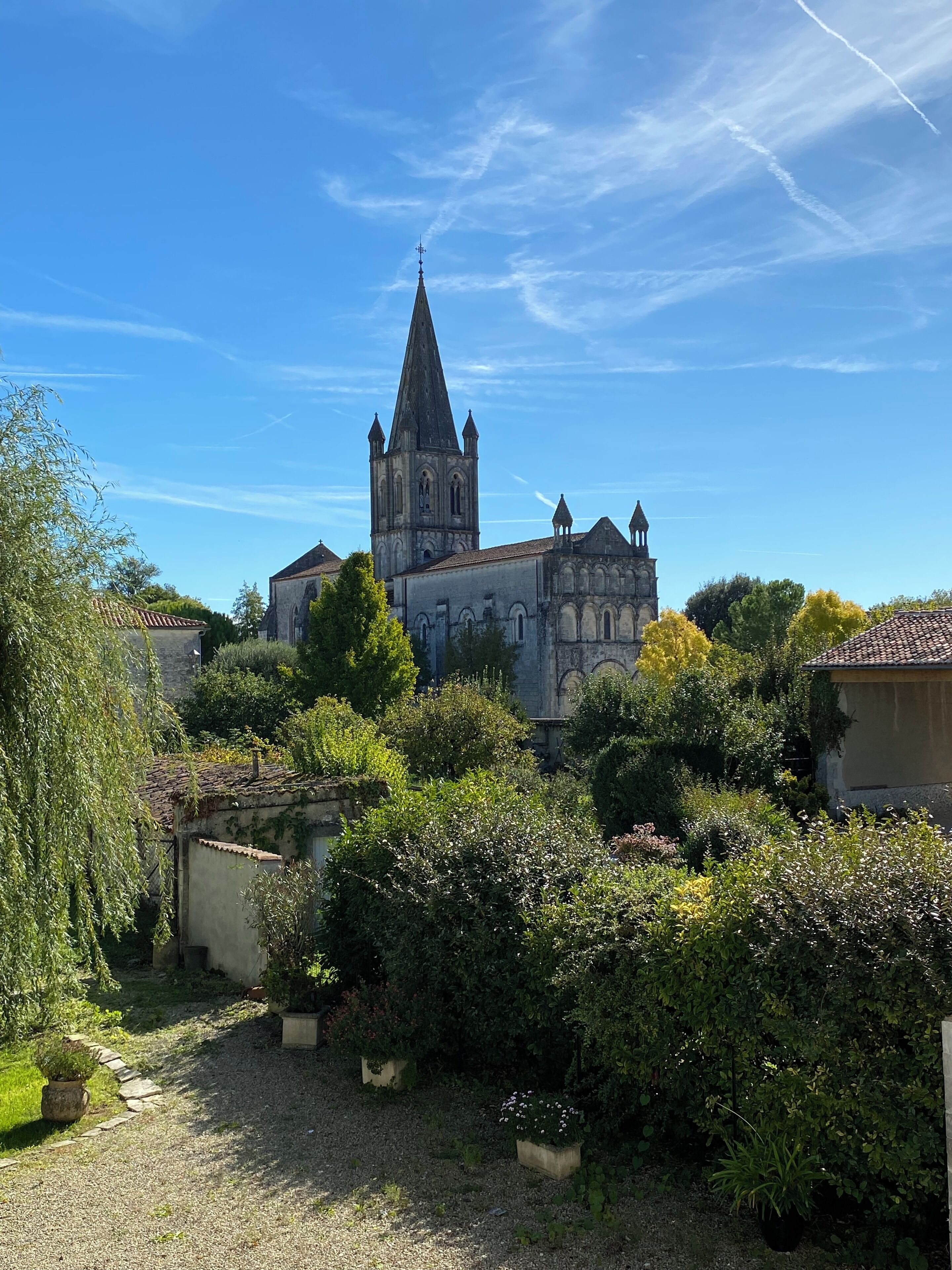 A historic church with a tall spire, surrounded by lush greenery and a gravel path.