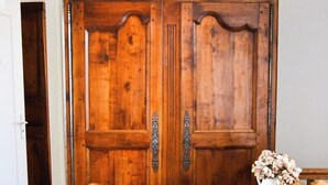 A wooden wardrobe with two doors, a small white vase with dried flowers, and a wooden chair in front.