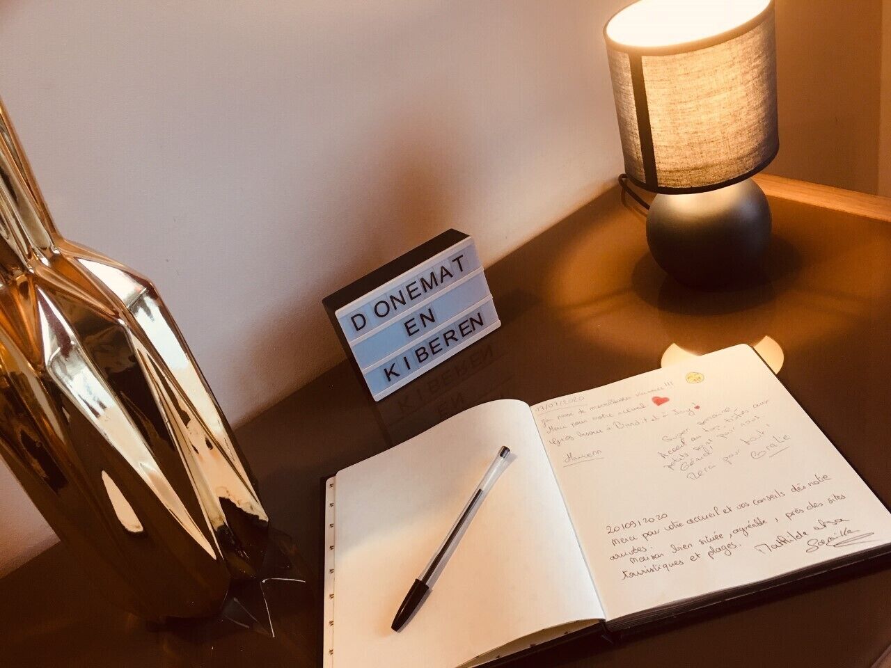 A notebook with a pen on a table, a lamp, and a sign that reads "D'ONET EN KIBEREN".