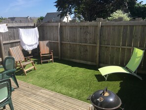 Um quintal com deck de madeira, churrasqueira e duas cadeiras de jardim.