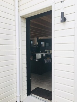 Uma porta que dá para um quarto, com moldura preta, parede externa branca e um tapete preto pequeno na entrada.