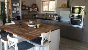A modern kitchen with a wooden island, white chairs, stainless steel appliances, and a window with blinds. - Pleasant house in Luberon with swimming pool, France (Viens)