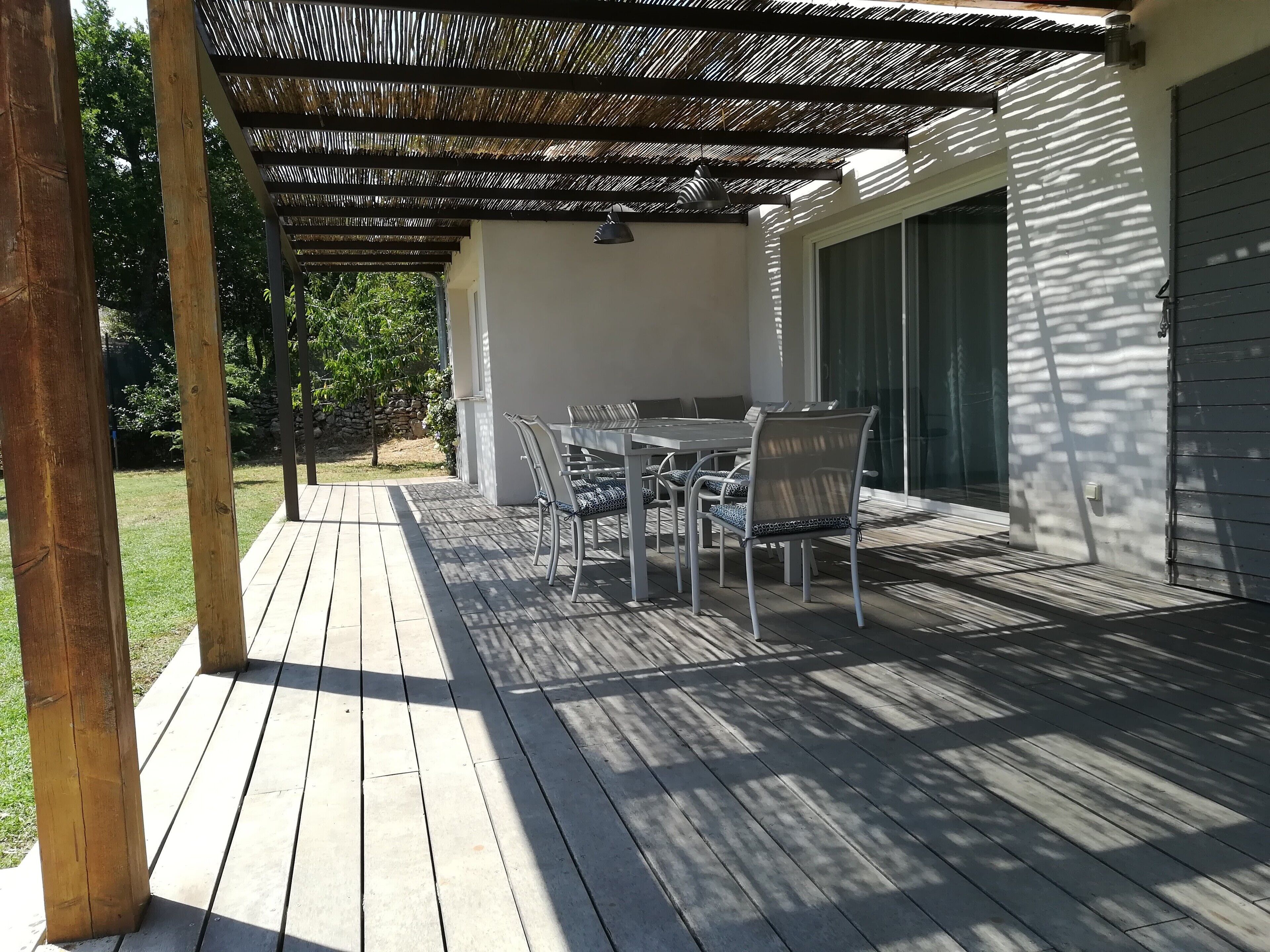Une terrasse couverte avec une table et des chaises, une pergola au-dessus et une vue sur le jardin arrière.