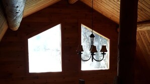 A wooden cabin with a sloped ceiling, a chandelier, and large windows.