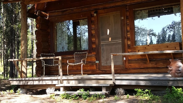 A rustic log cabin with a porch, large windows, and a chimney.
