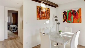 A modern dining area with a glass table, white chairs, and two abstract paintings on the walls. - T2 Marché de Forville CANNES (Cannes)
