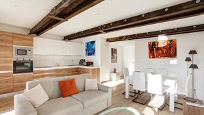 A modern living room with a sofa, a dining area with white chairs, a kitchen with wooden cabinets, and artwork on the walls. - T2 Marché de Forville CANNES (Cannes)