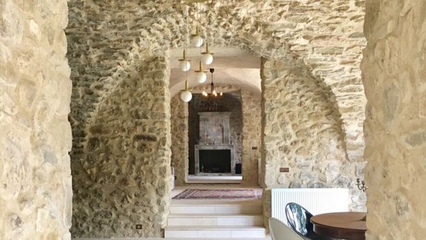 A stone-walled room with a fireplace, a dining table with chairs, and a chandelier.
