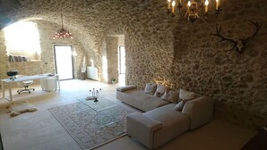 A stone-walled room with a sofa, a desk, and a chandelier.